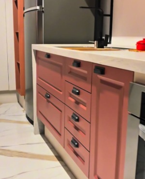 Cozinha planejada com armários em tom rosa terroso, puxadores pretos e bancada clara