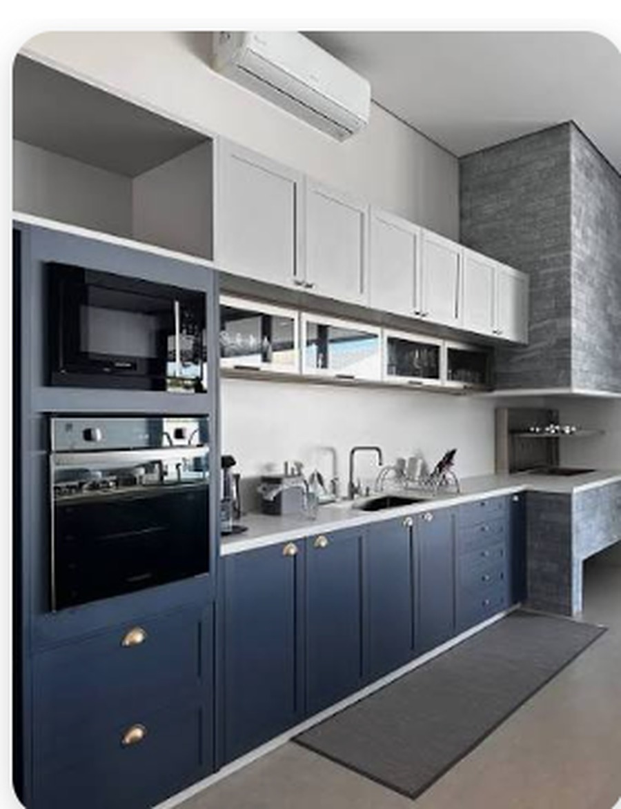 Cozinha planejada com armários inferiores em azul profundo, aéreos claros e bancada branca